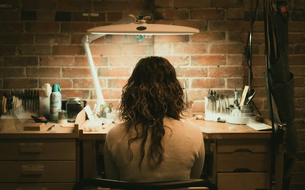 A jeweler working at a bench lit by a lamp